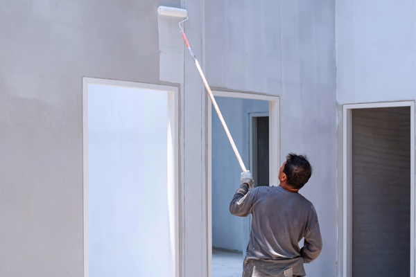 Artisan appliquant une peinture de protection blanche au rouleau sur une façade extérieure
